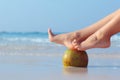 Female feet propped on coconut on sea background Royalty Free Stock Photo