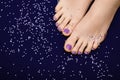 Female feet with purple pedicure. Woman legs with glitter purple nail design on purple fabric with purple paillettes