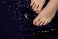 Female feet with purple pedicure. Woman legs with glitter purple nail design on purple fabric with golden paillettes