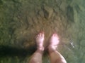 Female feet with red nails stand in the clear water on the stony bottom of a river