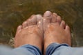 Female feet in running water. Close-up of female legs wearing jeans and resting while wetting her feet. RTY