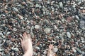Female feet in sea water on a pebble shore top view in summer, many pebbles, copy space, relaxation in nature, swimming in sea