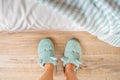 Female feet in soft blue slippers on a wooden floor near the bed close-up. Concepts of cozy fleece home shoes and warm domestic Royalty Free Stock Photo