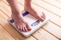 Female feet standing on mechanical scales for weight control on wooden background. Concept of slimming and weight loss