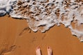 Female feet standing on the sand with ocean waves rolling Royalty Free Stock Photo