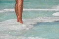 Female feet on stone, covered with salt formations between waves in water. Crystallization salt on stone, spatherapy in Dead Sea