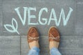 Female feet with text vegan written on grey sidewalk