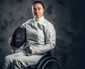 Female fencer in wheelchair holds safety mask and a sword.