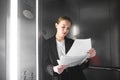 Female financial analyst holding papers studying documents standing in the elevator. Ambitious businesswoman is reading carefully