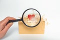 Female fingers hold a magnifying glass over a red heart in a box. A symbol of the great importance of human kindness Royalty Free Stock Photo