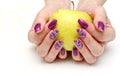 Female fingers with painted nails hold a yellow apple. lilac nails with a pattern Royalty Free Stock Photo