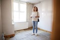 Female First Time Buyer Looking At House Survey In Room To Be Renovated