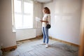 Female First Time Buyer Looking At House Survey In Room To Be Renovated