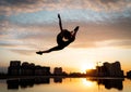 Female flexible dancer jumping during sunset on cityscape background with reflection in the water. Concept of freedom Royalty Free Stock Photo