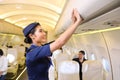 Female flight attendant closing the overhead luggage compartment lid after all passengers are seated