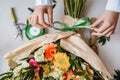 a female florist ties a green ribbon bow on a bouquet of flowers wrapped in craft paper on the desktop. Top view. Royalty Free Stock Photo