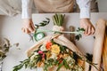 a female florist ties a green ribbon bow on a bouquet of flowers wrapped in craft paper on the desktop. Top view. Royalty Free Stock Photo