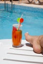 Female foot in front of the pool with drink on a d