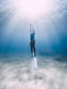 Female freediver dive with fins underwater in ocean with sunlight