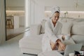 Female freelancer in bathrobe relaxing on sofa at home and working remotely on laptop Royalty Free Stock Photo