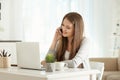 Female freelancer talking by phone while working on laptop in home office Royalty Free Stock Photo