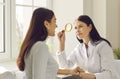 Female friendly doctor examining face skin of young smiling woman patient using magnifying glass Royalty Free Stock Photo