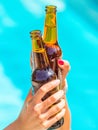 Female friends cheer clinking bottles of beer in their hands next to a pool of blue water