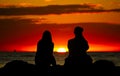 Female friends or couple in silhouette enjoying the brilliant red sunset on seashore rocks during summer travel Royalty Free Stock Photo