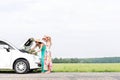 Female friends examining broken down car on country road against clear sky Royalty Free Stock Photo