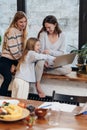 Female friends and a little girl are sitting at home on a windowsill watching a series.