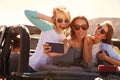 Female Friends On Road Trip In Convertible Car Taking Selfie