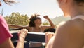 Female Friends Standing Up Through Sun Roof Car And Dancing On Road Trip Through Countryside Royalty Free Stock Photo