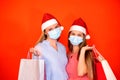 Female friends wearing surgical mask and Christmas hat holding shopping bags on a vivid red orange background Royalty Free Stock Photo