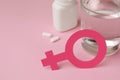 Female gender sign, pills and glass of water on pink background, closeup. Space for text