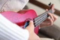 female gentle hands in which lies a red wooden ukulele, close-up. hipster girl hobby, at home