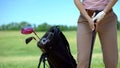Female golfer holding iron club, ready to play game, bag with iron clubs nearby Royalty Free Stock Photo