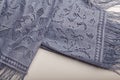 Female grey lace shawl with fringe and flowers ornaments on white table background. Clothing and accessories
