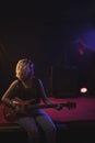 Female guitarist playing guitar while sitting on stage Royalty Free Stock Photo