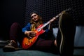 Female guitarist sitting on the floor in a recording Studio. A woman plays music on a red electric guitar. Denim jacket, cap, Royalty Free Stock Photo