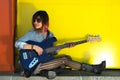 Female guitarist sitting on ledge playing blue guitar