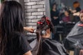 Female hairdresser brushing and drying using hand held blow dryer on hair of young brunette woman Royalty Free Stock Photo