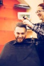 Female hairdresser is cutting hair of bearded smiling man client Royalty Free Stock Photo