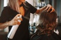 Female hairdresser fixing customer woman hair with spray and put care treatment while styling curls