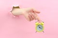 A female hand through the background holds a yellow retro alarm clock. At 15.55 hours, the concept of a seven-hour working day.