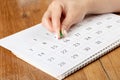 A female hand with a beautiful manicure holds a green pushpin to mark the date on the calendar 16 day Royalty Free Stock Photo