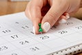 A female hand with a beautiful manicure holds a green pushpin to mark the date on the calendar 25 day Royalty Free Stock Photo