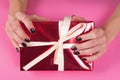 Female hand with black nails manicure on red gift box with white bow on pink background, close up Royalty Free Stock Photo