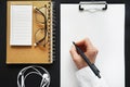 Female hand with a black pen over a blank sheet of paper next to notepads, white wired headphones and glasses Royalty Free Stock Photo