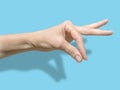 Female hand on blue background with shadow. The thumb and forefinger are assembled into a pinch. communication symbols an