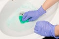 Female hand in a blue glove wipes the sink with a green foam sponge in the bathroom Royalty Free Stock Photo